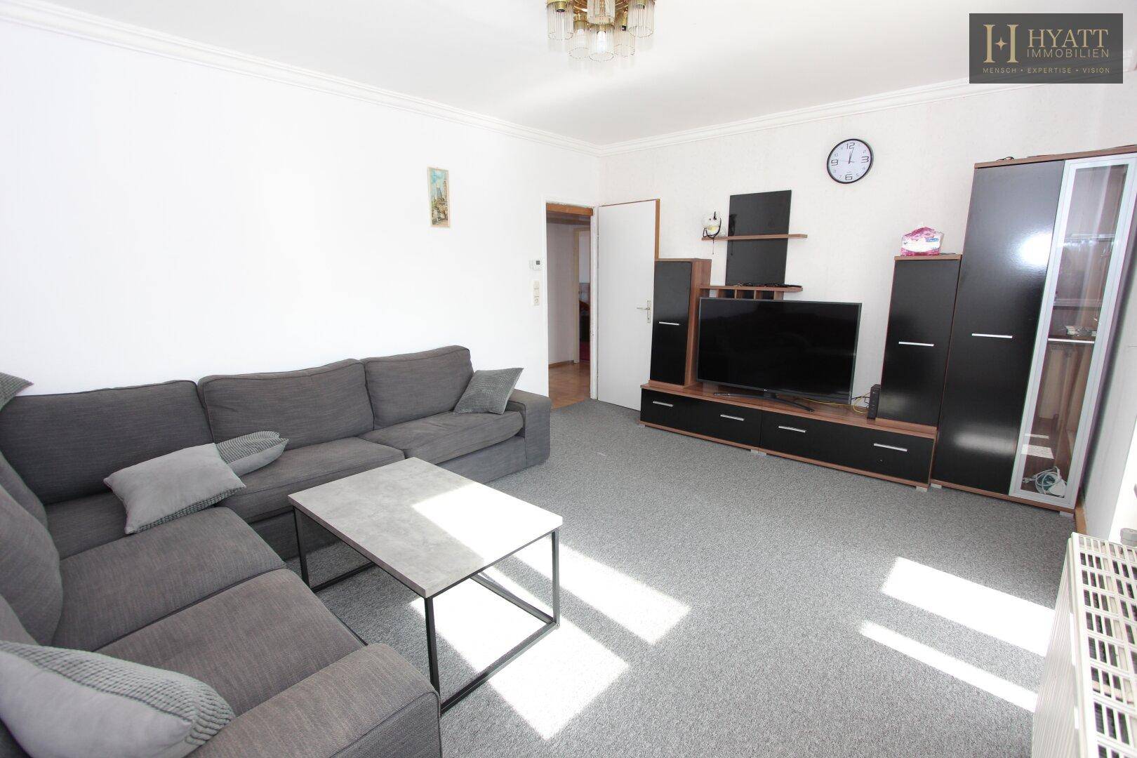 Geräumiges Wohnzimmer mit grauem Teppichboden, großem Sofa und modernen TV-Möbeln.