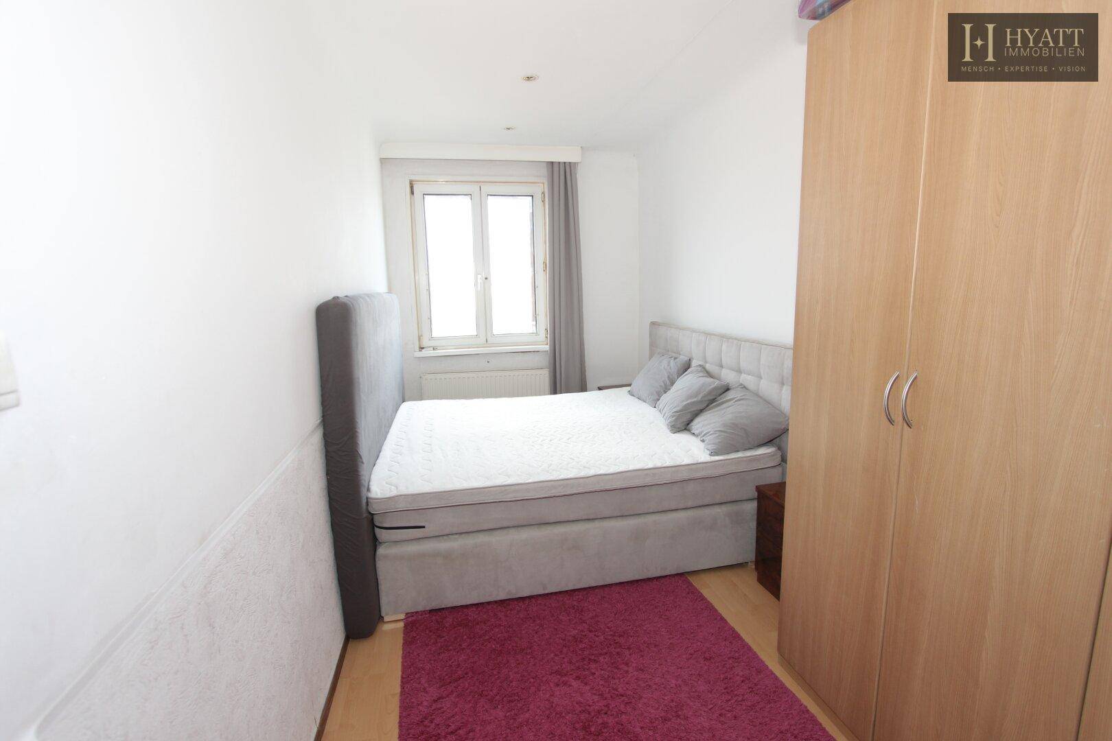 Schlafzimmer mit Doppelbett, hellem Holzschrank und Parkettboden, gut beleuchtet.