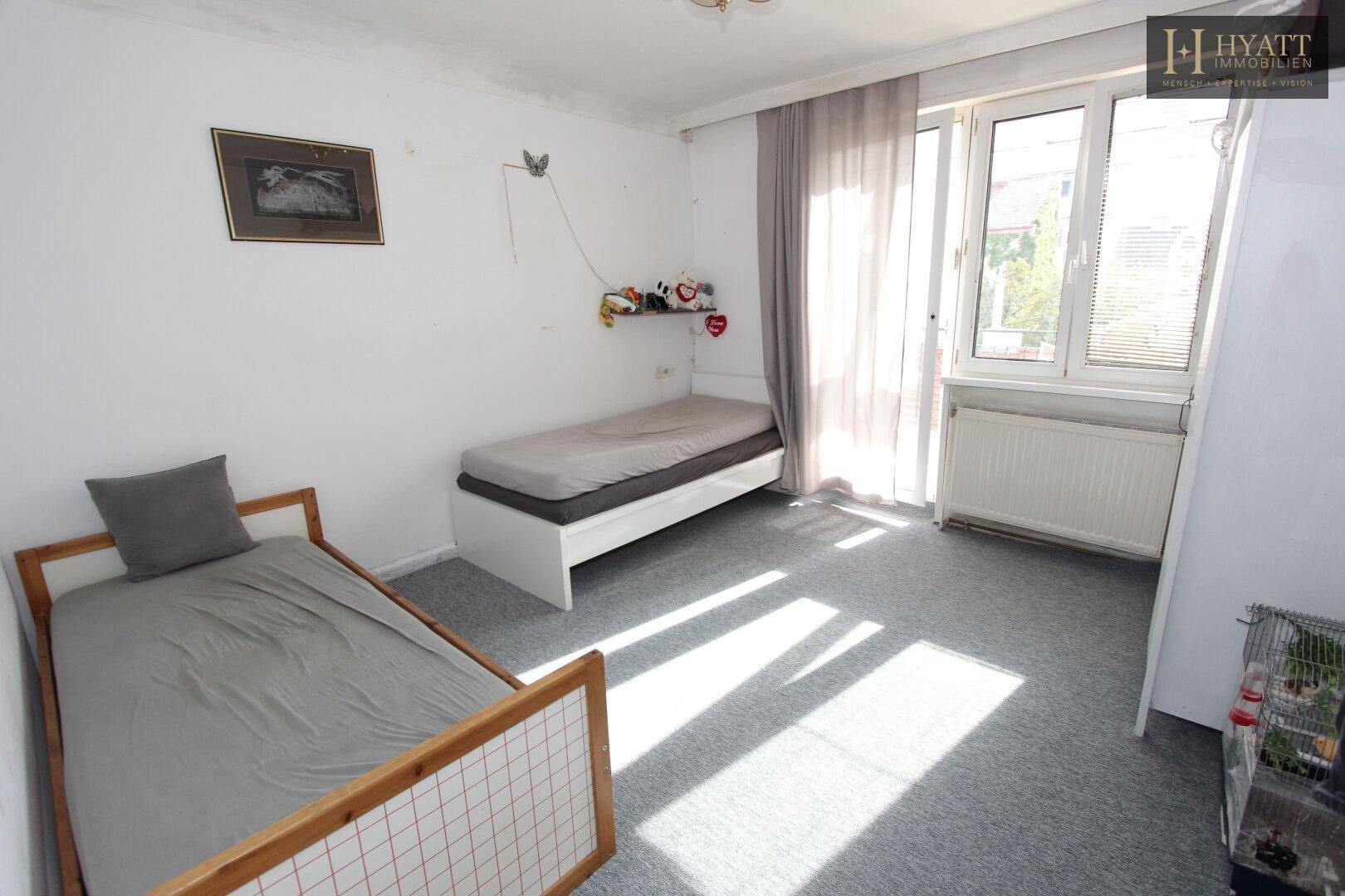 Kinderzimmer mit zwei Einzelbetten, Teppichboden und Zugang zu einem sonnigen Balkon.
