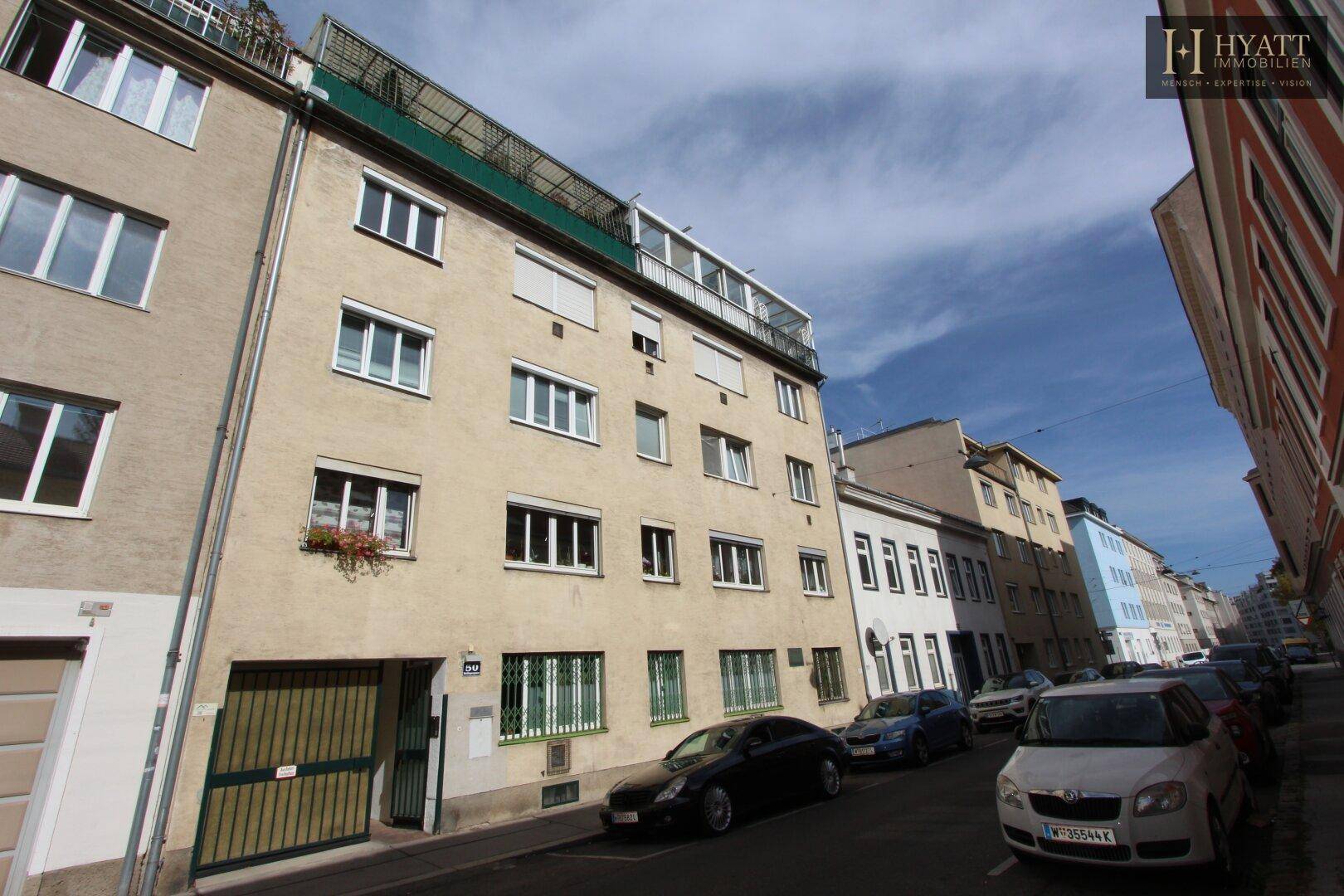 Wohngebäude in einer städtischen Straße mit parkenden Autos und blauem Himmel.