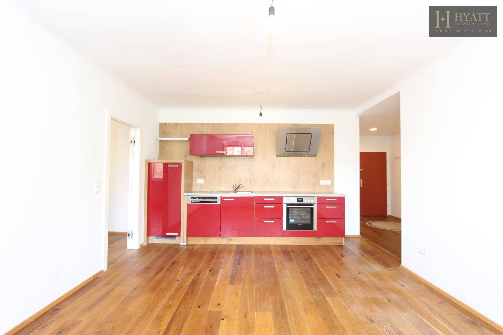 Moderne Küchenzeile mit roten Fronten, integrierten Geräten und Holzboden in offenem Wohnbereich.
