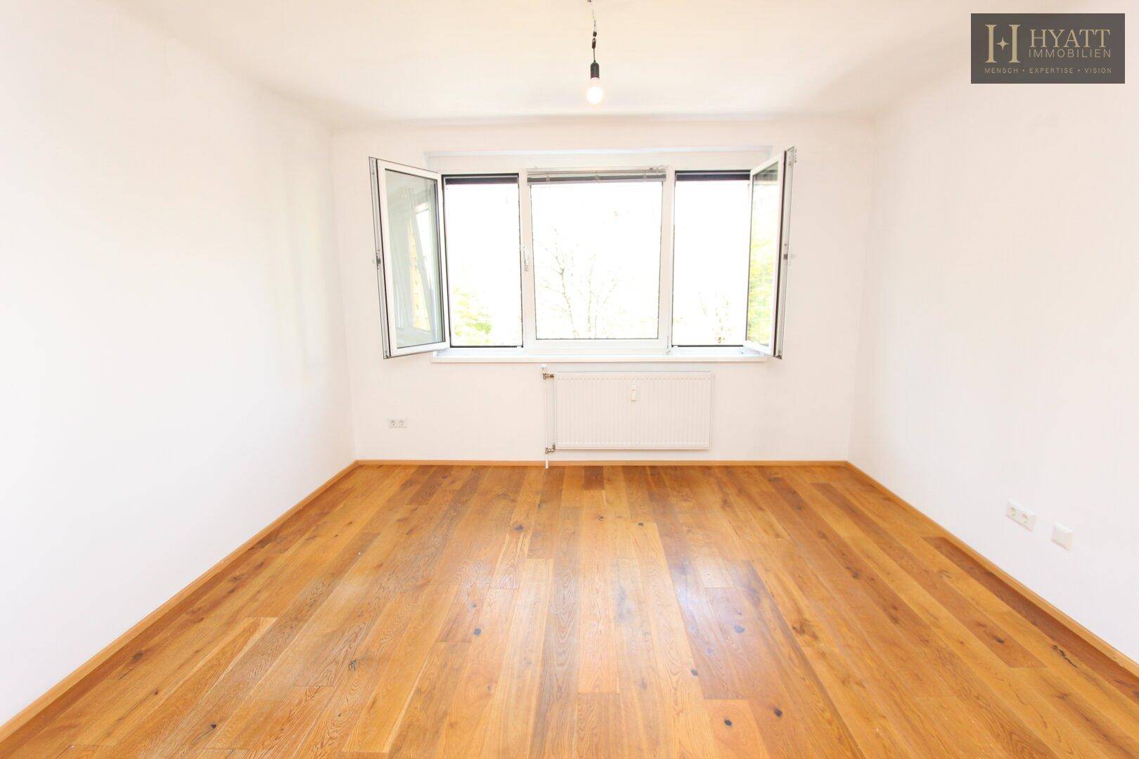Helles Schlafzimmer mit großen Fenstern und warmem Holzboden, bereit zur individuellen Gestaltung.