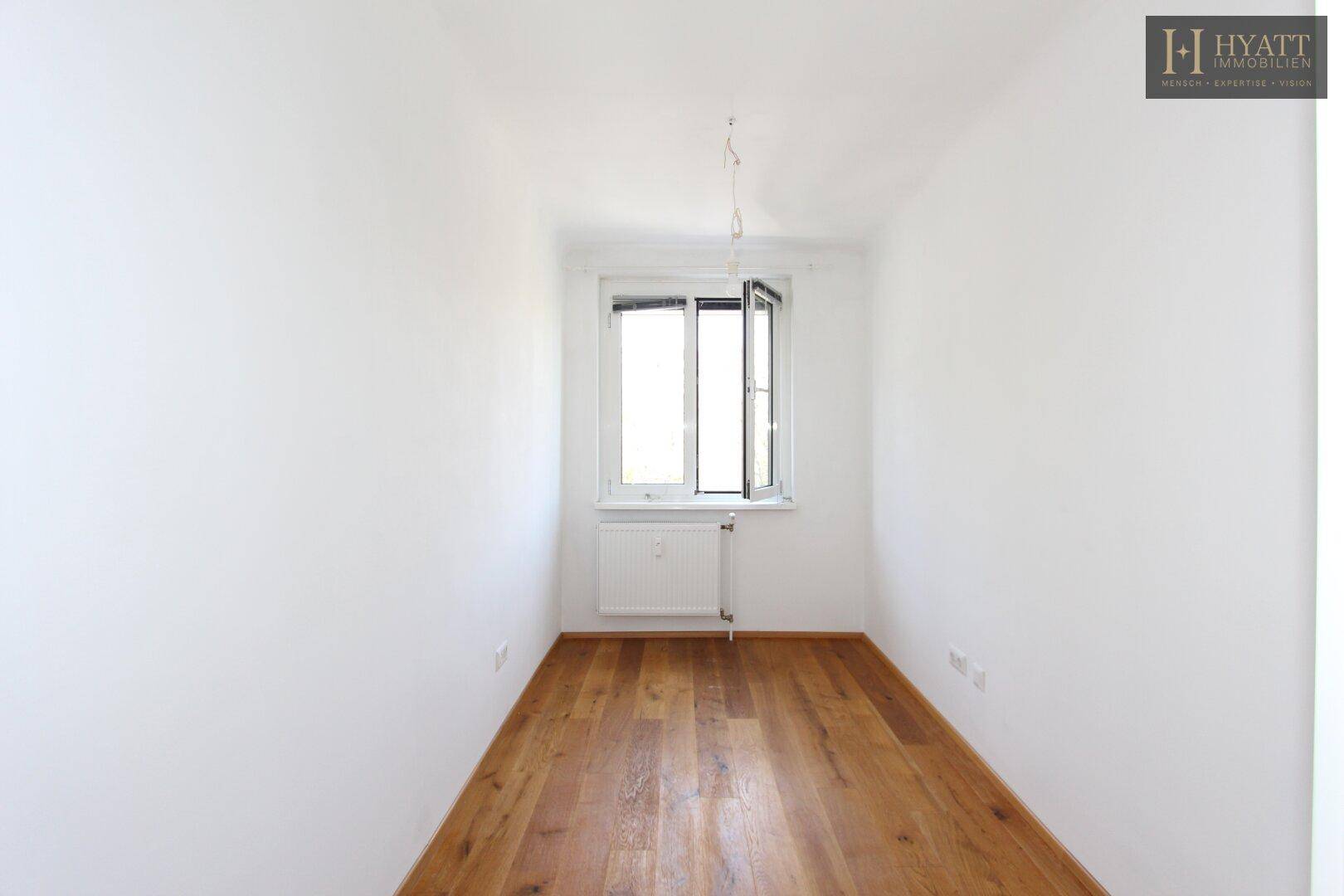 Kleines, helles Zimmer mit Holzboden und Fenster, ideal als Kinderzimmer oder Arbeitsbereich.