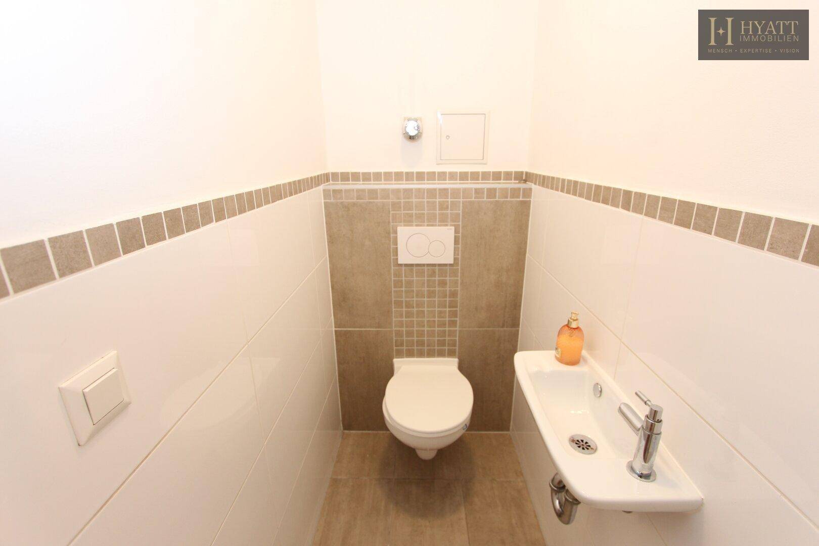 Kompaktes Gäste-WC mit Wand-WC, kleinem Waschbecken und modernen Fliesen.