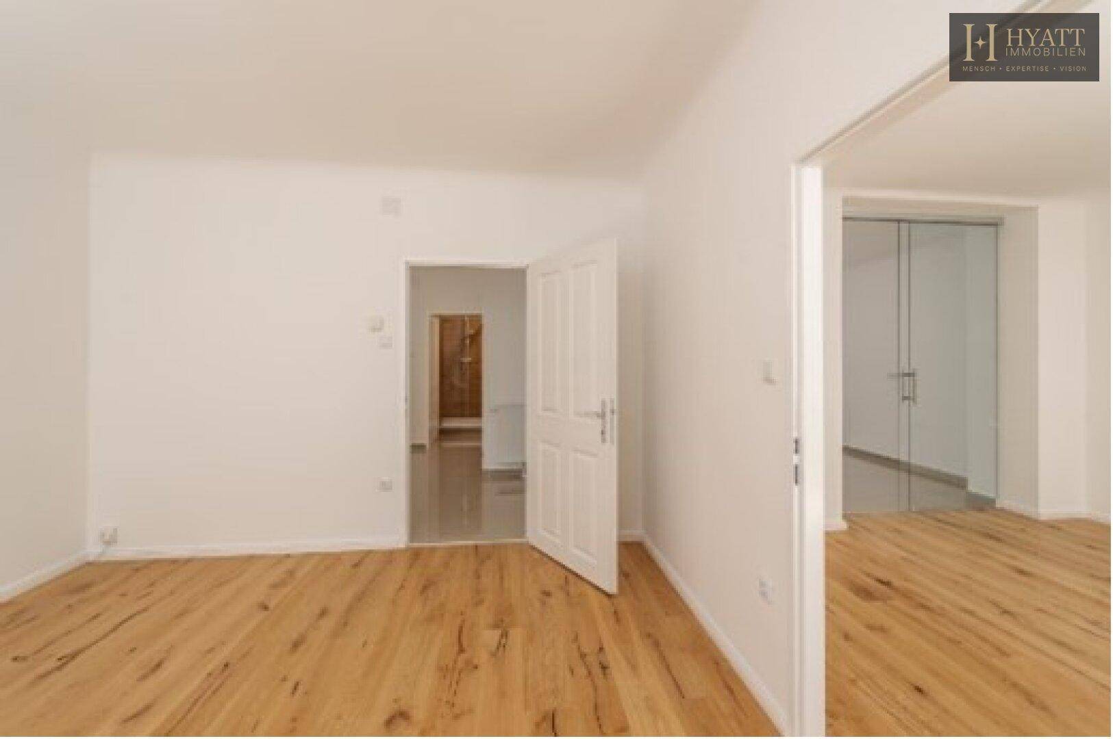 Heller, leerer Raum mit Holzboden und mehreren Türen, die zu anderen Bereichen führen.