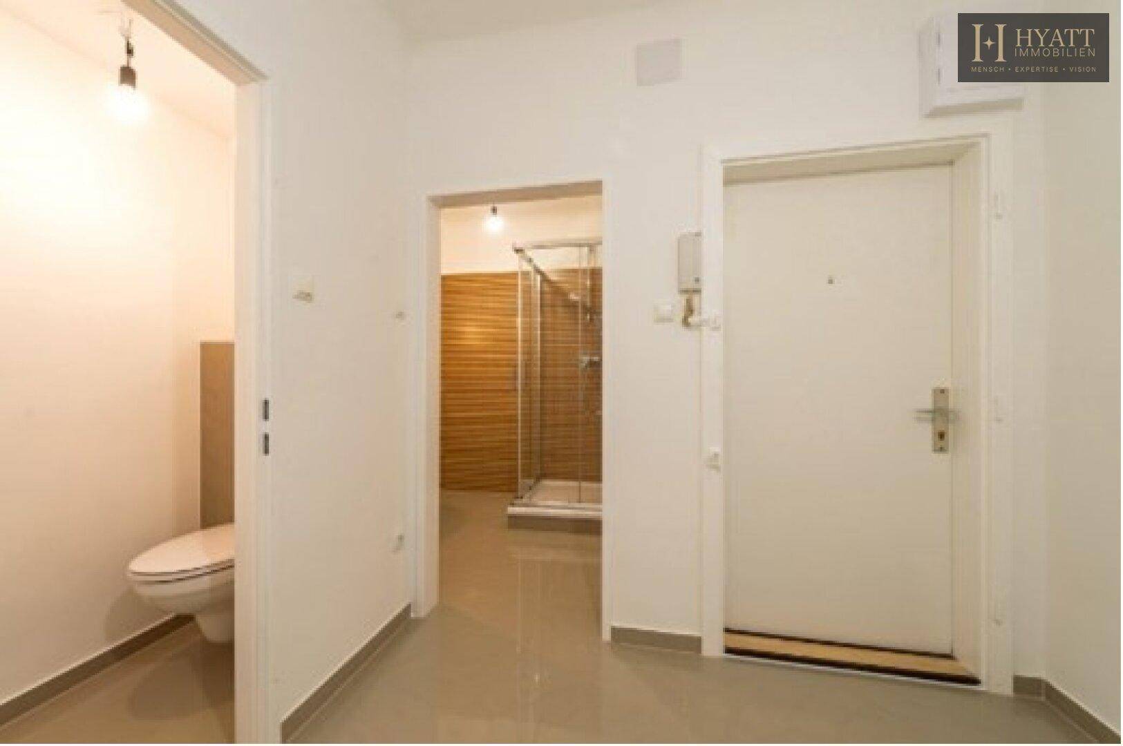 Eingangsbereich mit Fliesenboden, der zu einem WC und einem Badezimmer mit Dusche führt.
