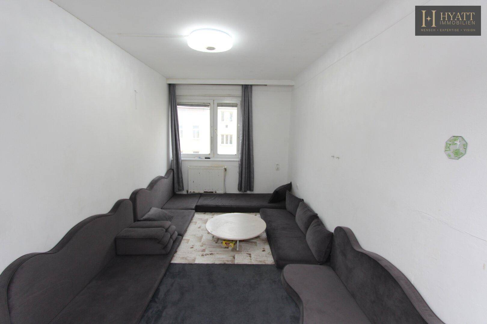 Geräumiges Wohnzimmer mit dunklen Sofas und einem runden Couchtisch, bereit zur individuellen Gestaltung.