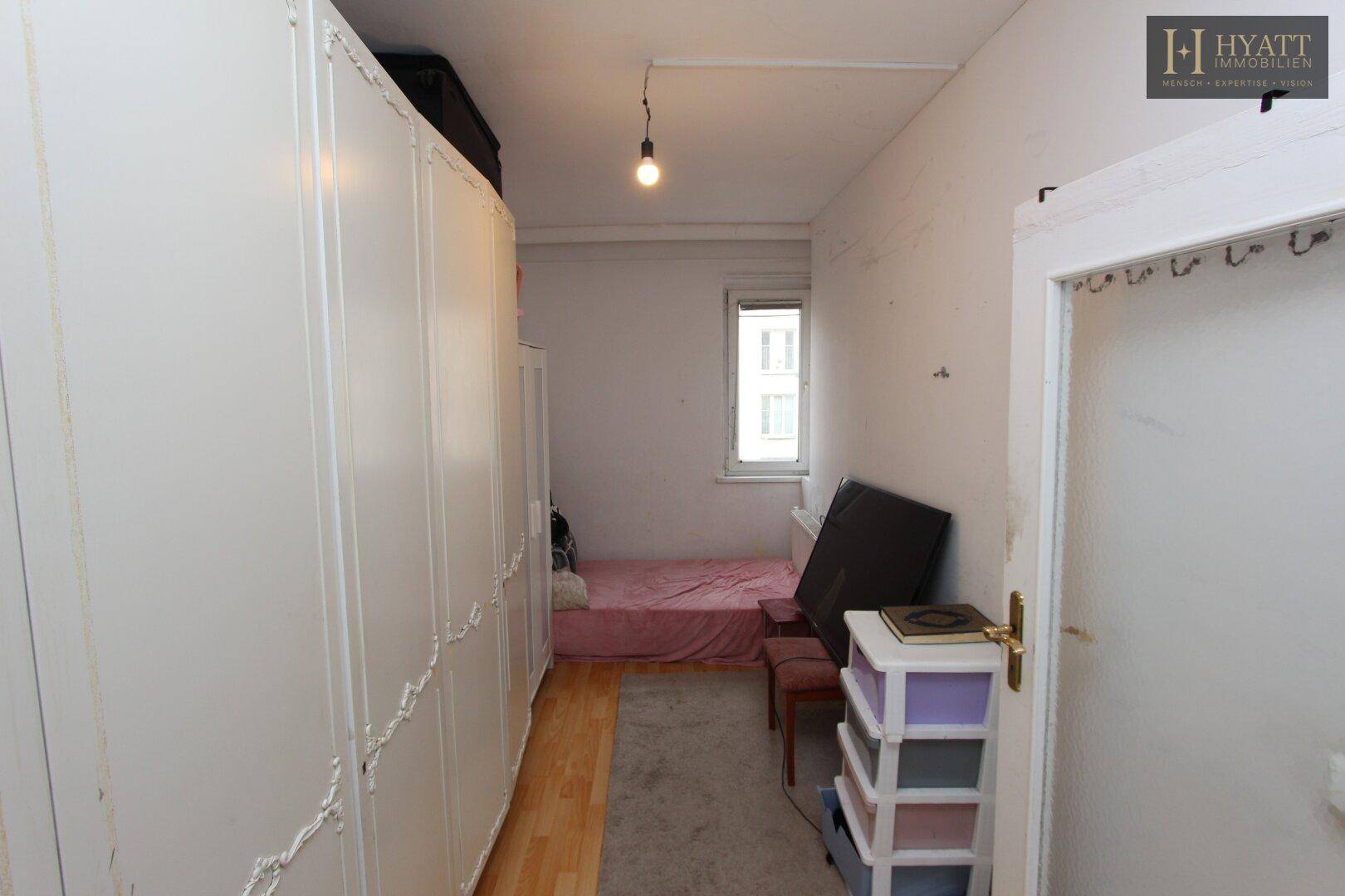 Schlichtes Schlafzimmer mit Einzelbett und großem Kleiderschrank, mit Holzboden.