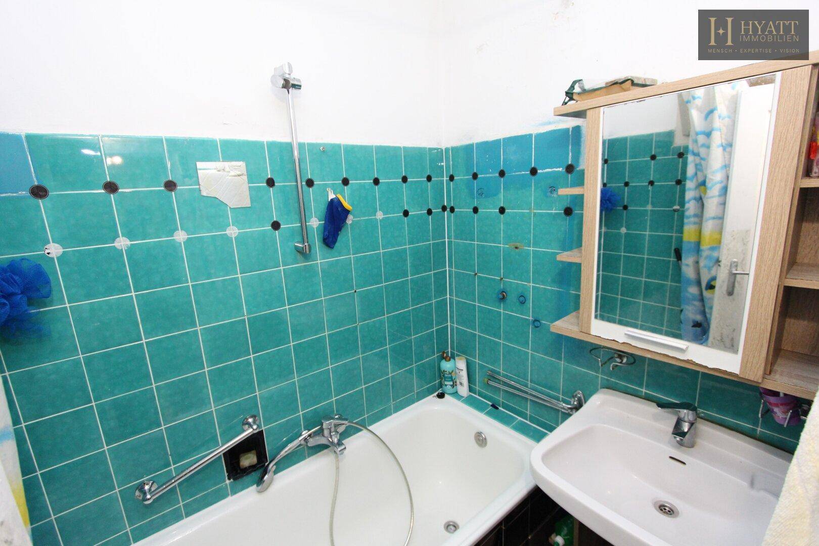 Badezimmer mit türkisfarbenen Fliesen, Badewanne und Waschbecken, im Stil der 80er Jahre.