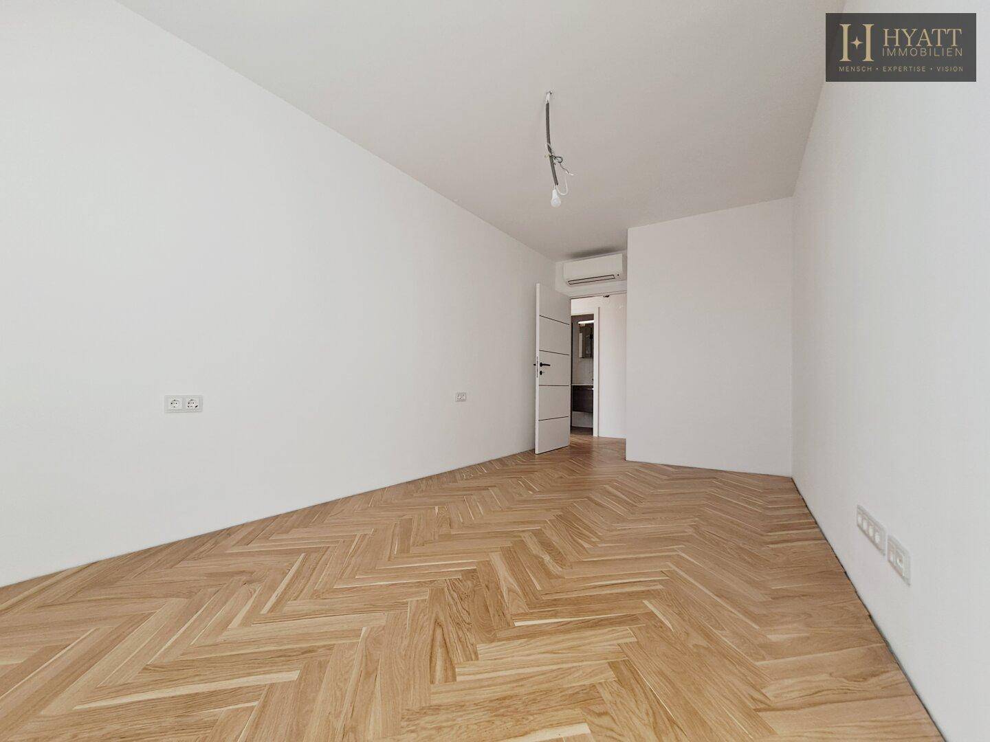 Helles, leeres Schlafzimmer mit Fischgrätparkett und weiß gestrichenen Wänden.