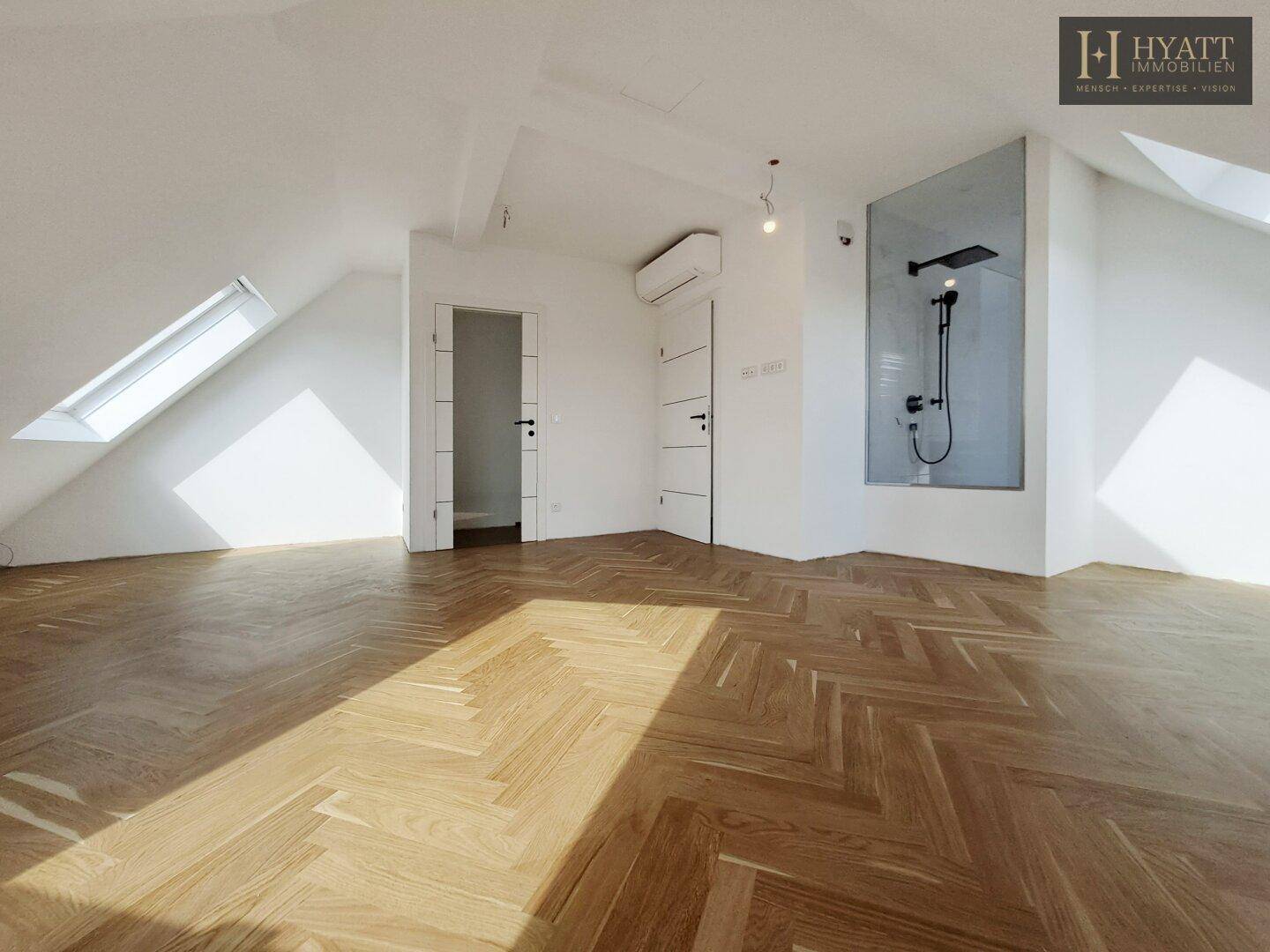 Geräumiges, leeres Schlafzimmer mit Fischgrätparkett, Dachfenstern und offener Dusche.