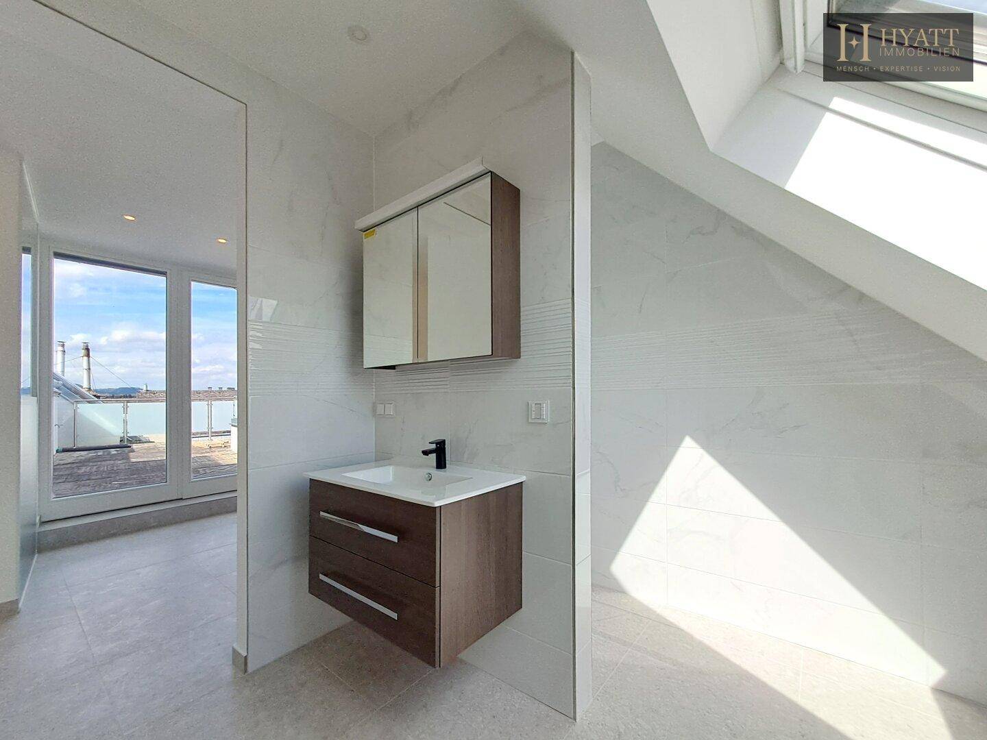 Helles Badezimmer mit Waschtisch, Spiegelschrank und Zugang zur Terrasse.