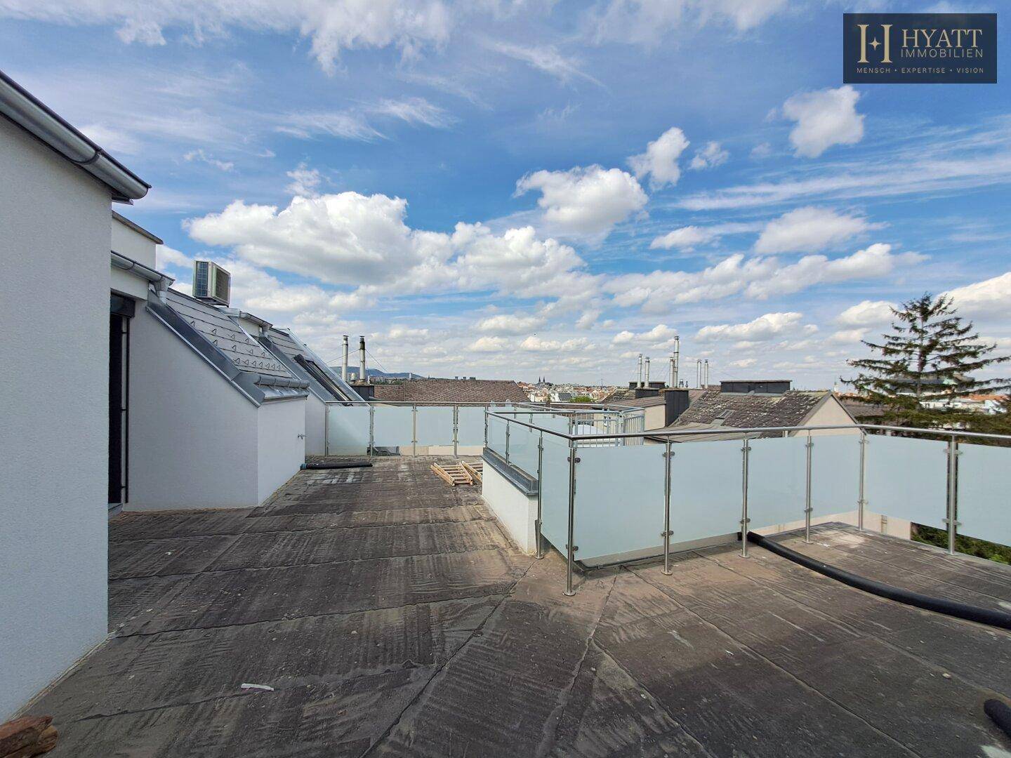 Geräumige, unmöblierte Dachterrasse mit Glasgeländer und Panoramablick über die Stadt.