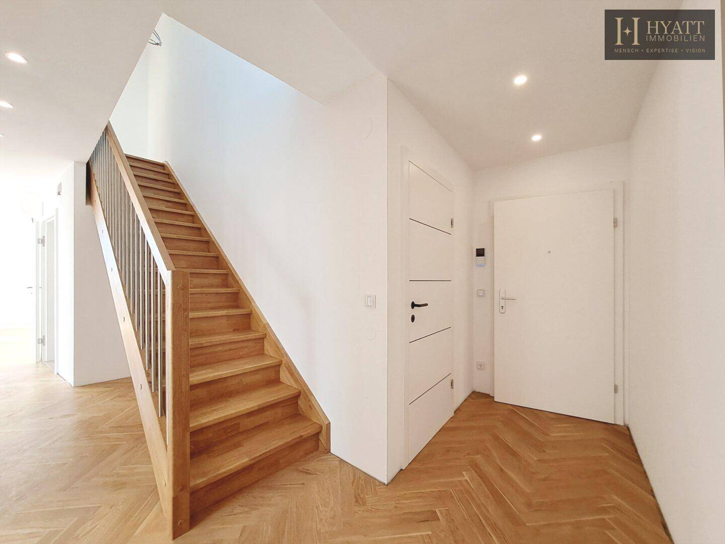 Heller Eingangsbereich mit Holztreppe und Fischgrätparkettboden.