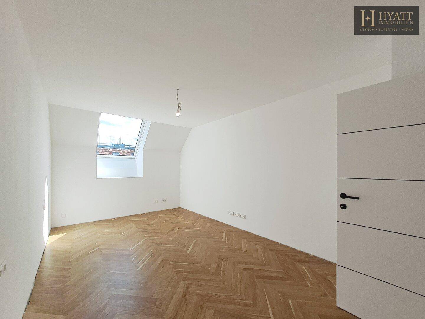 Heller, leerer Raum mit Fischgrätparkett und Dachfenster, vielseitig nutzbar.