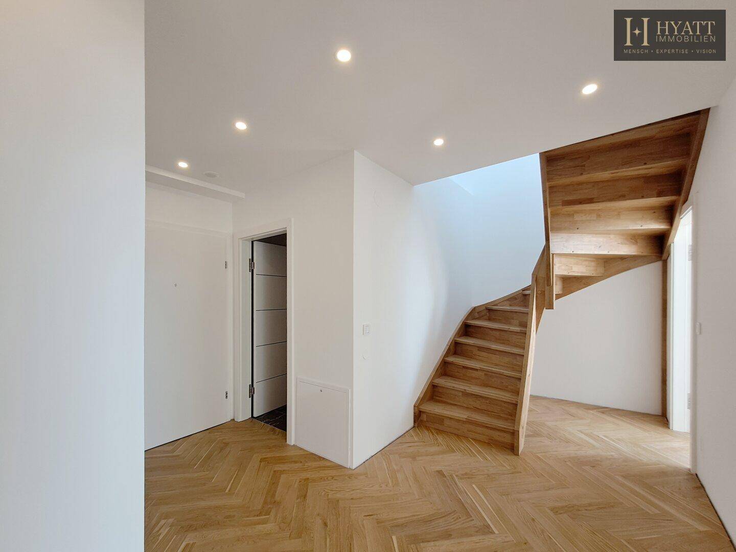 Geräumiger Flur mit elegantem Fischgrätparkett und einer modernen Holztreppe, die in die obere Etage führt.