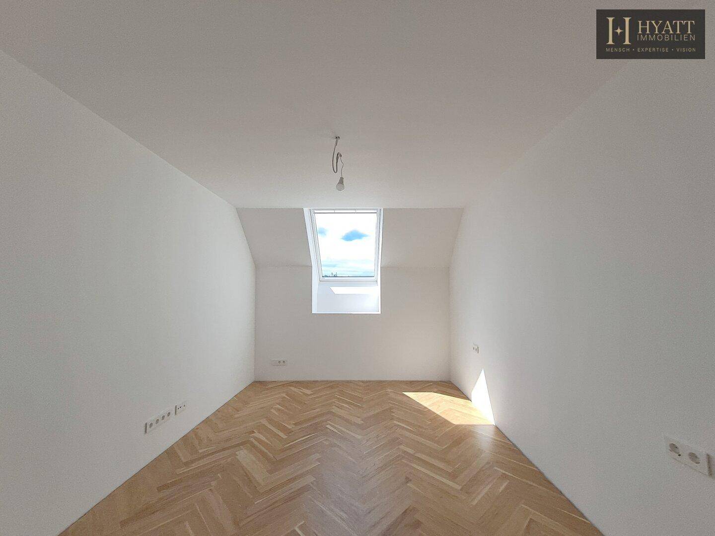 Heller Raum mit Fischgrätparkett, weißen Wänden und einem Dachfenster, ideal als Schlafzimmer.