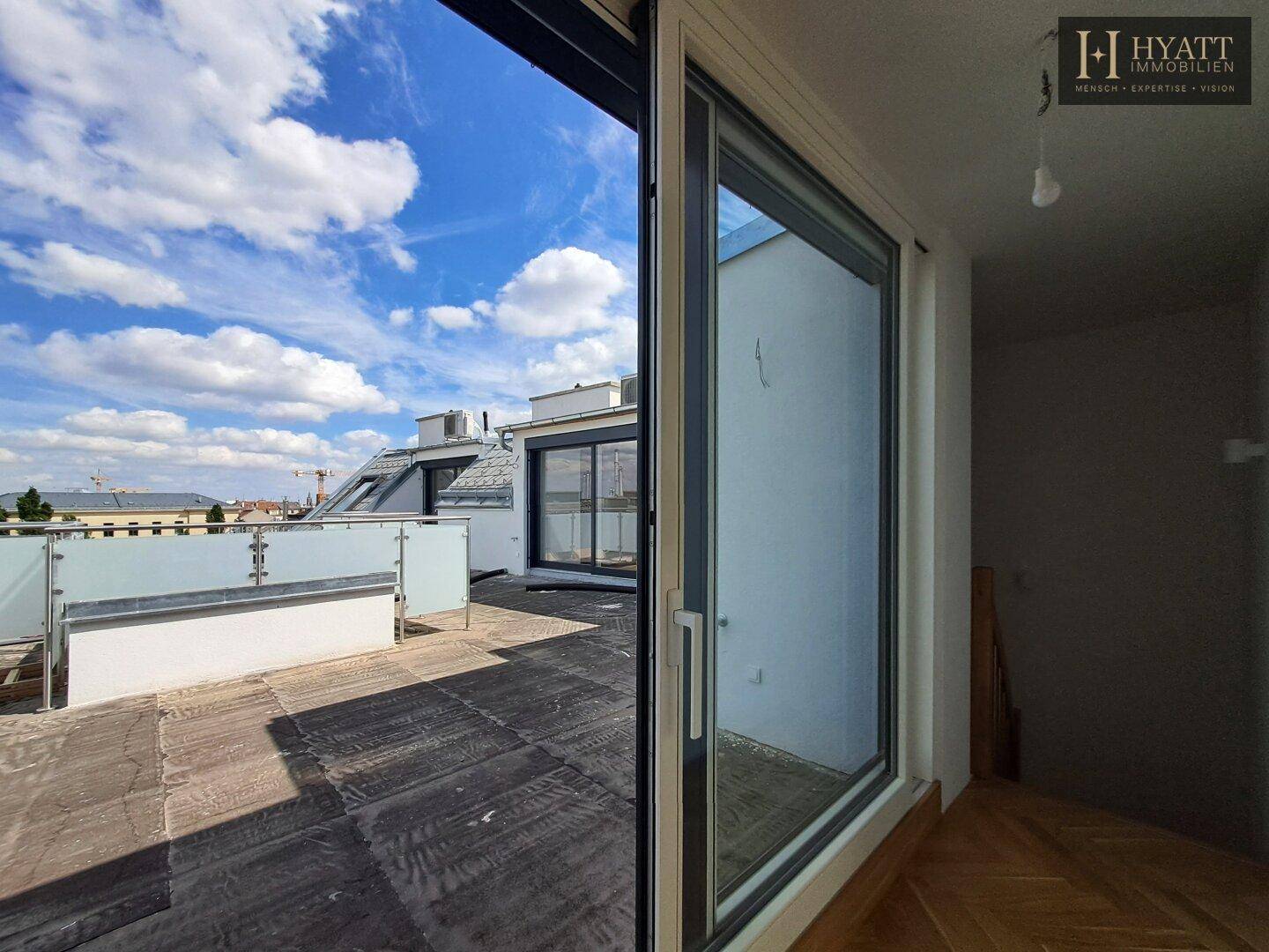 Große, unmöblierte Dachterrasse mit Glasgeländer und weitem Stadtblick, verbunden mit einem Innenraum.