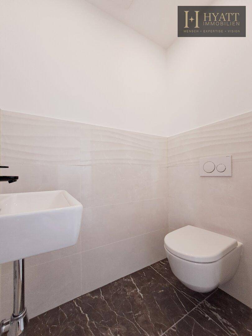 Helles Gäste-WC mit wandhängender Toilette, kleinem Waschbecken und modernen weißen Fliesen.