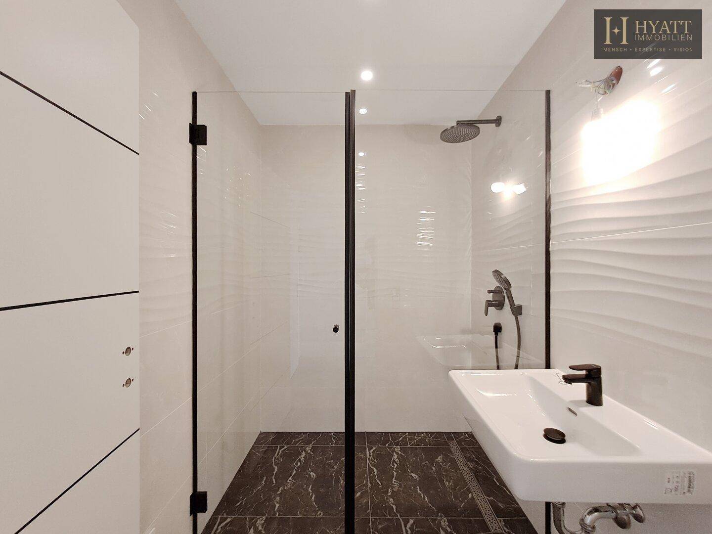 Modernes Badezimmer mit begehbarer Dusche, eleganten weißen Fliesen und dunklem Boden, ausgestattet mit einem Einzelwaschbecken.