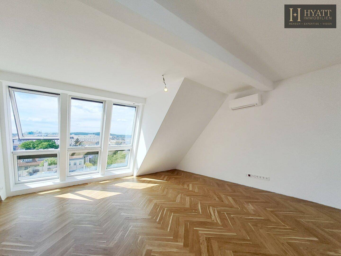 Geräumiges, leeres Wohnzimmer mit Fischgrätparkett und großen Fenstern.