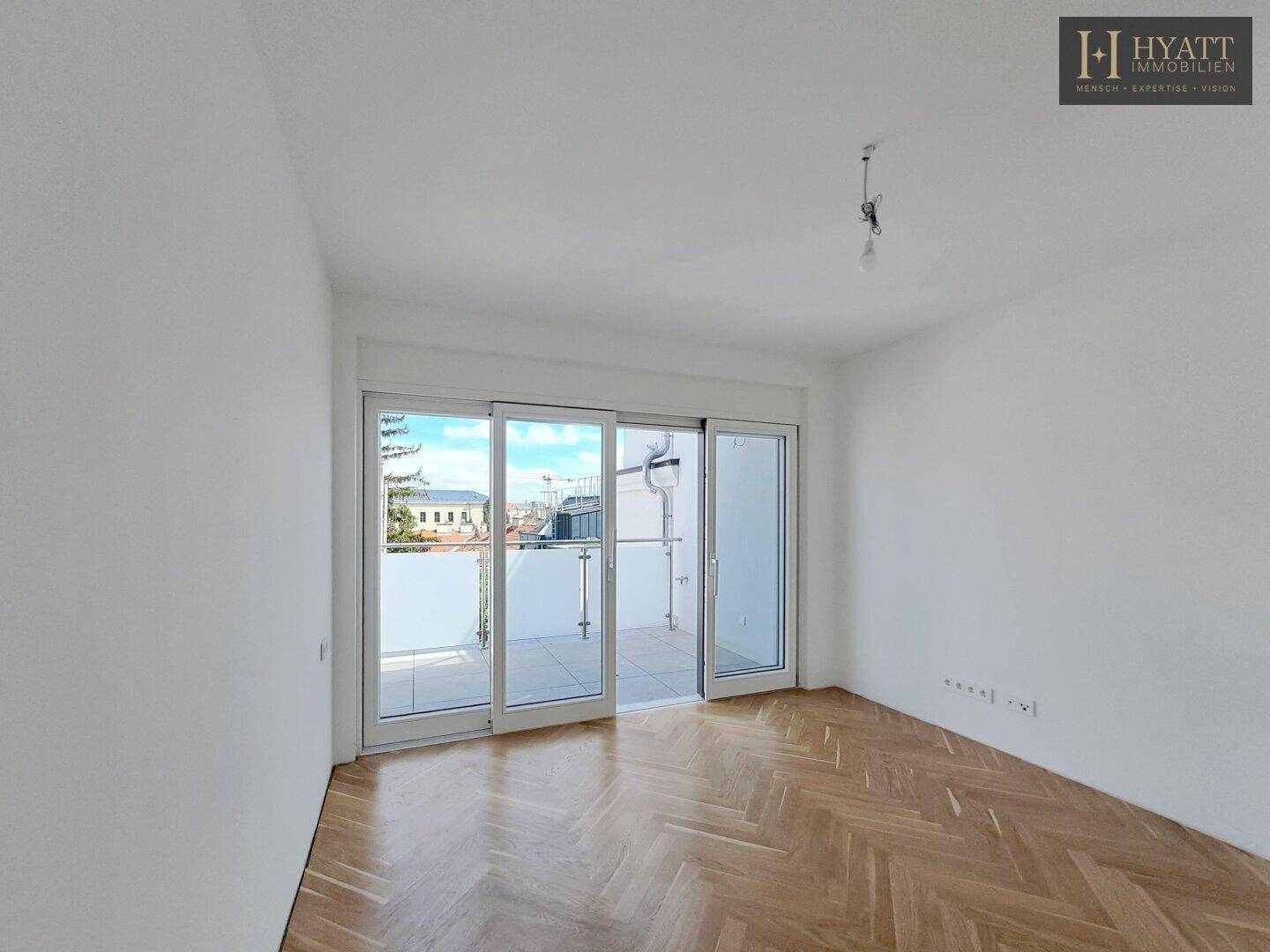 Helles, leeres Schlafzimmer mit Fischgrätparkett und Zugang zum Balkon.