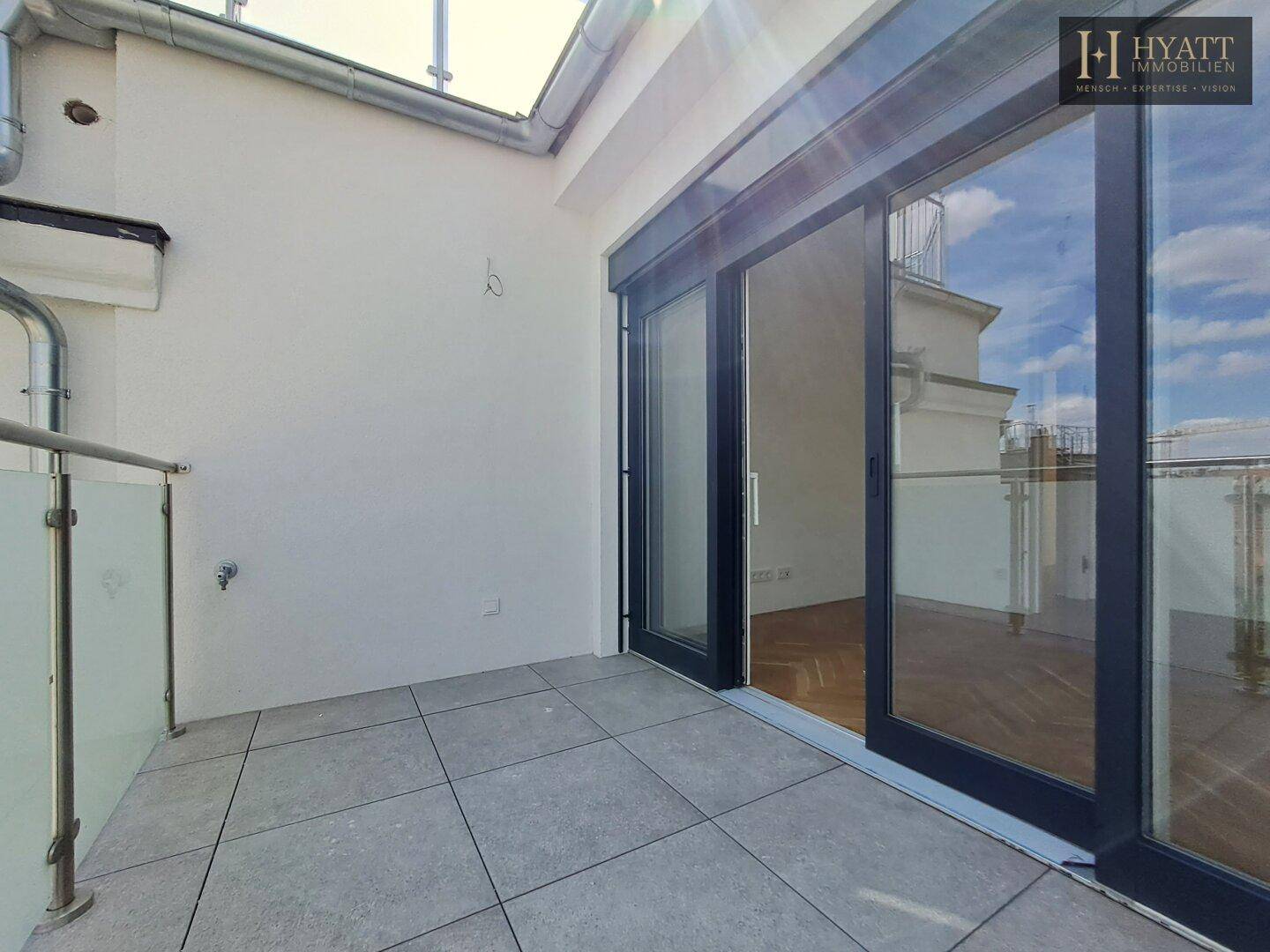 Leere Terrasse mit Fliesenboden und Schiebetüren zum Innenbereich.
