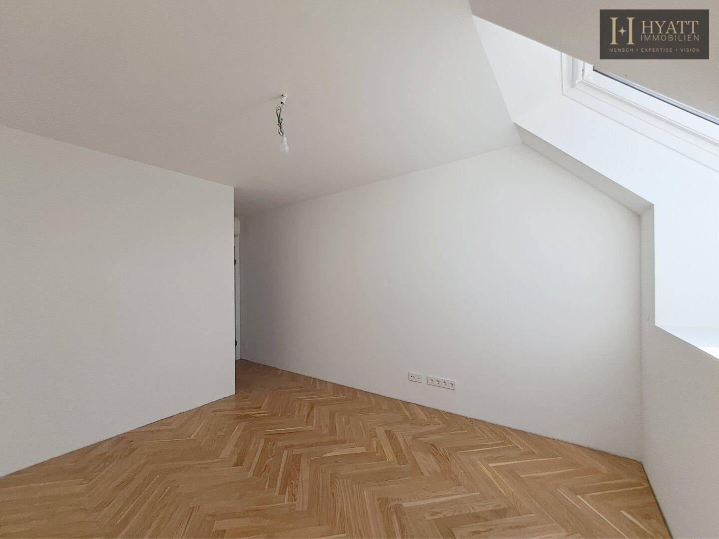 Leerer Raum mit Fischgrätparkett und Dachfenster, ideal als Büro.