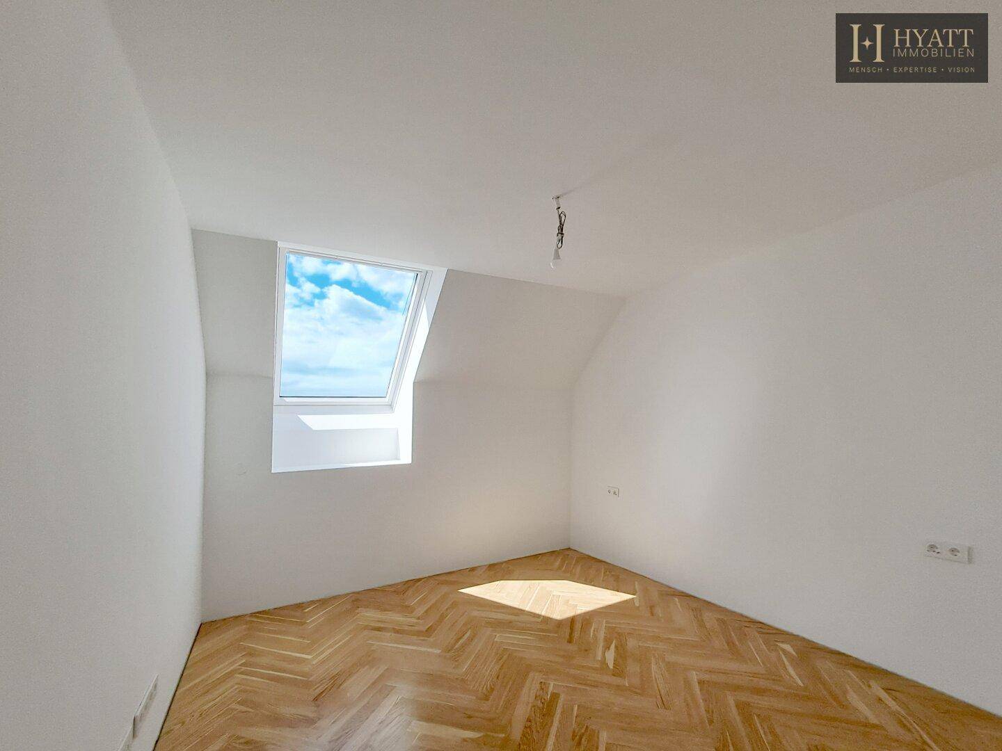 Leerer Raum mit Fischgrätparkett und Dachfenster, vielseitig nutzbar.
