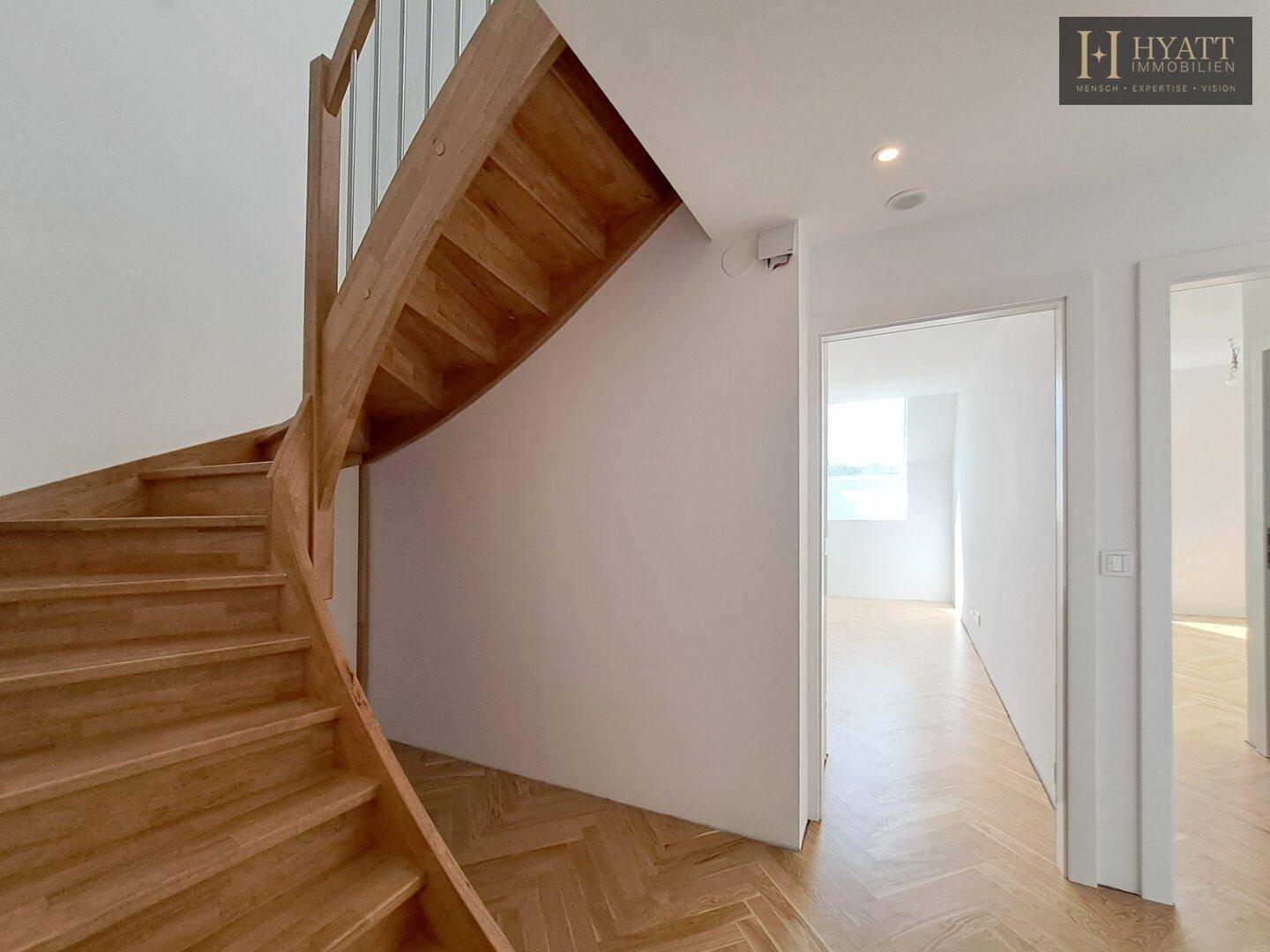 Heller Flur mit Holztreppe und Fischgrätparkett, verbindet die Ebenen.