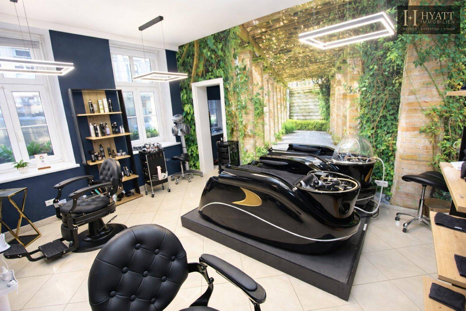 Moderner Friseur- und Spa-Bereich mit speziellen Liegen, großen Fenstern und einer grünen Wandtapete mit Pflanzenmotiv.