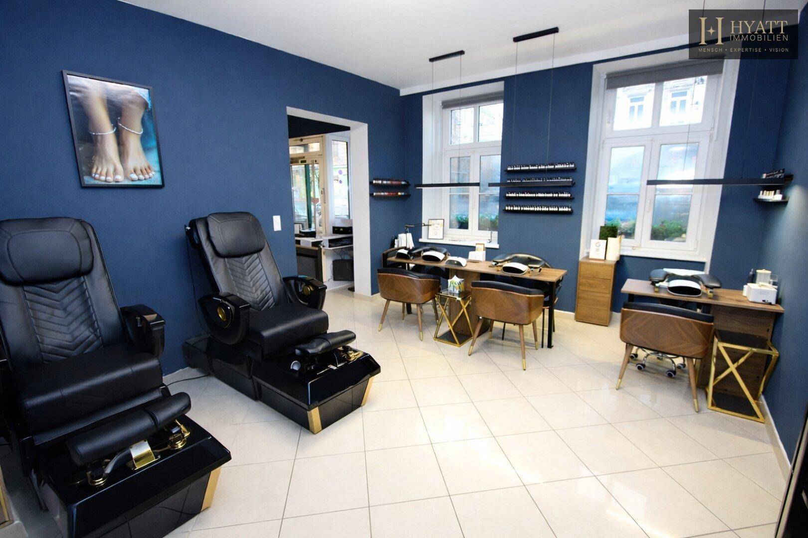 Geräumiger Schönheitssalon mit mehreren Maniküre- und Pediküre-Stationen, großen Fenstern und hellem Fliesenboden.