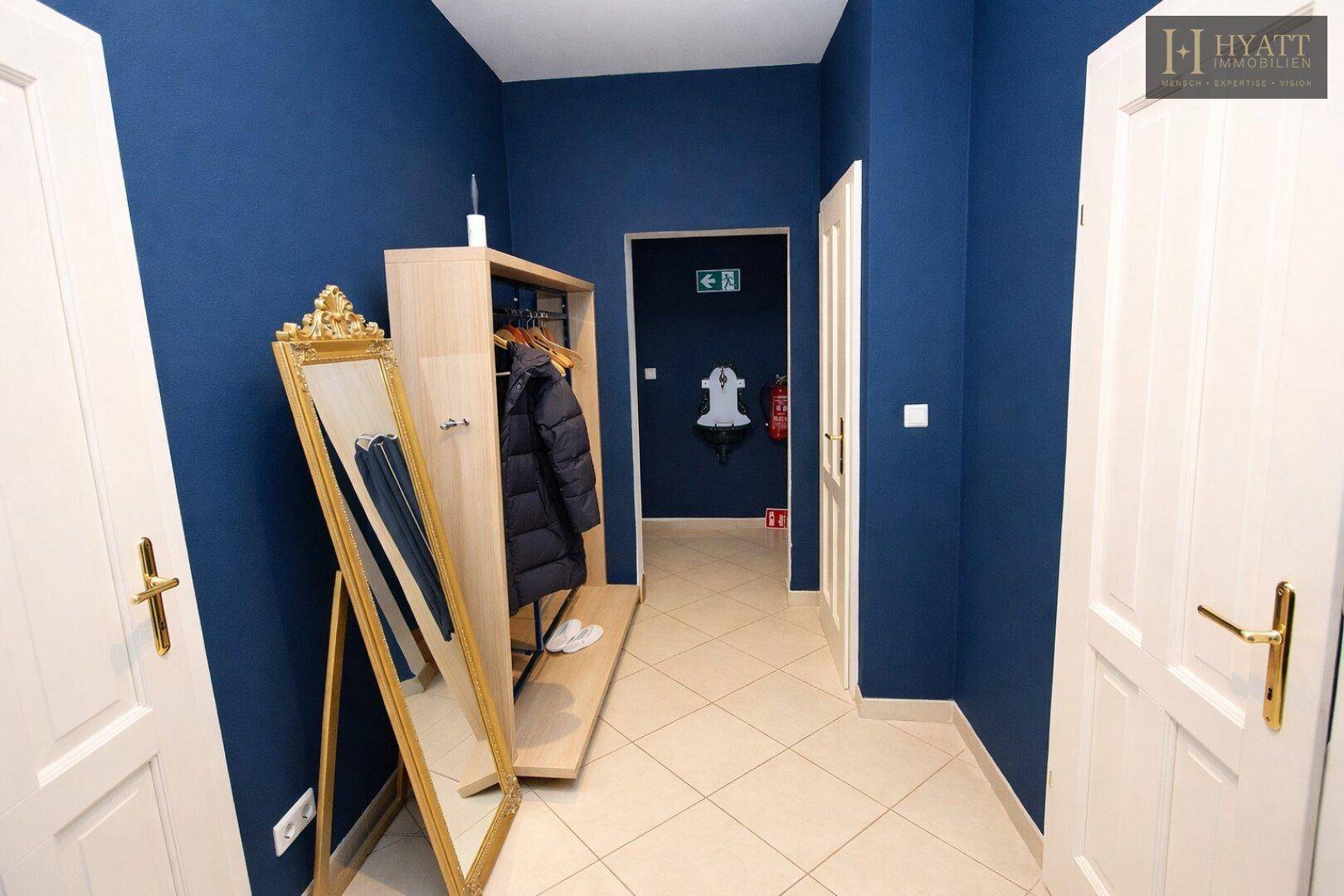 Heller Flur mit blauen Wänden, einem großen Spiegel und einer Garderobe.