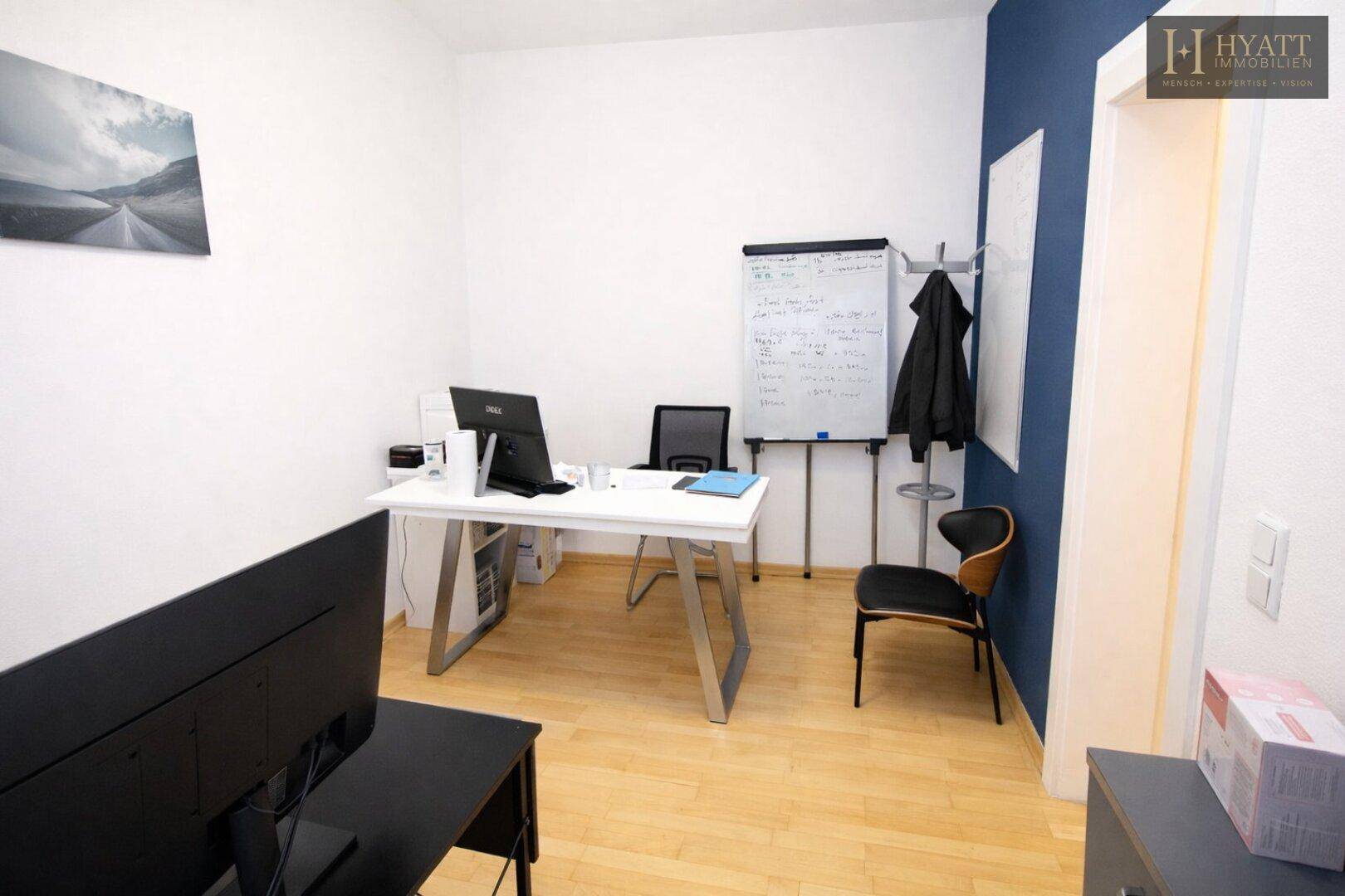 Modernes Büro mit hellem Holzboden, Schreibtisch und Flipchart, ideal für Besprechungen.