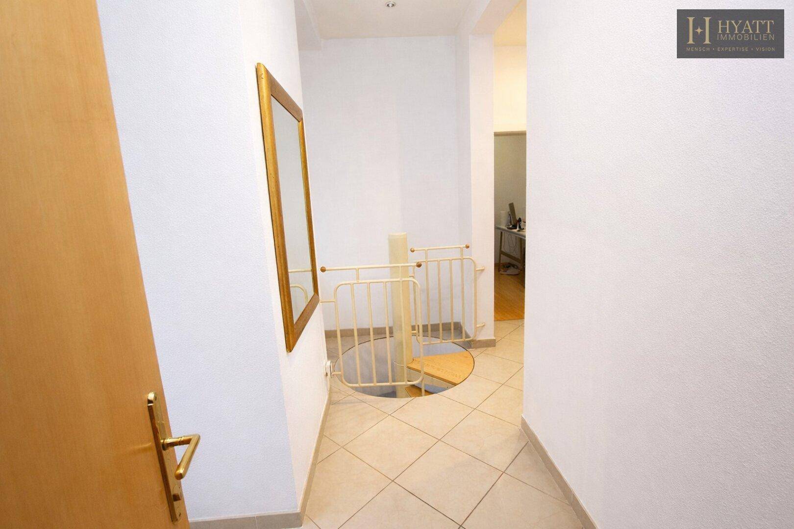 Heller Flur mit Fliesenboden und einem gesicherten Zugang zu einer Wendeltreppe.