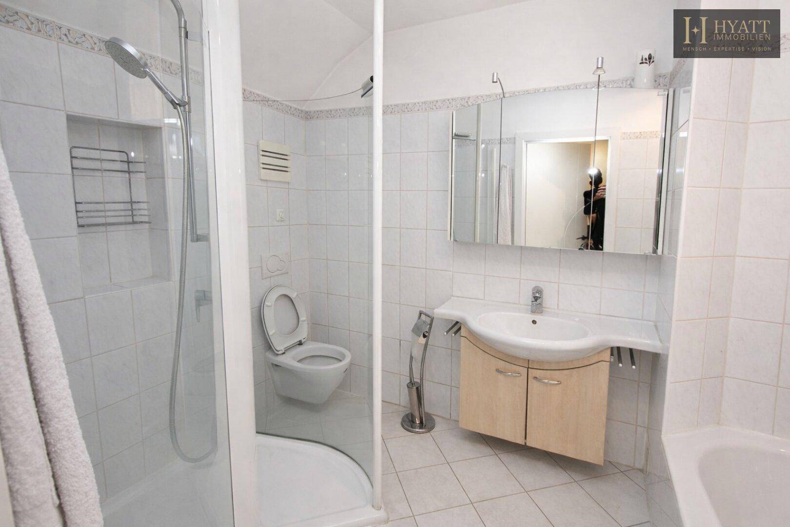 Helles Badezimmer mit Duschkabine, WC und Waschbeckenunterschrank, komplett gefliest.