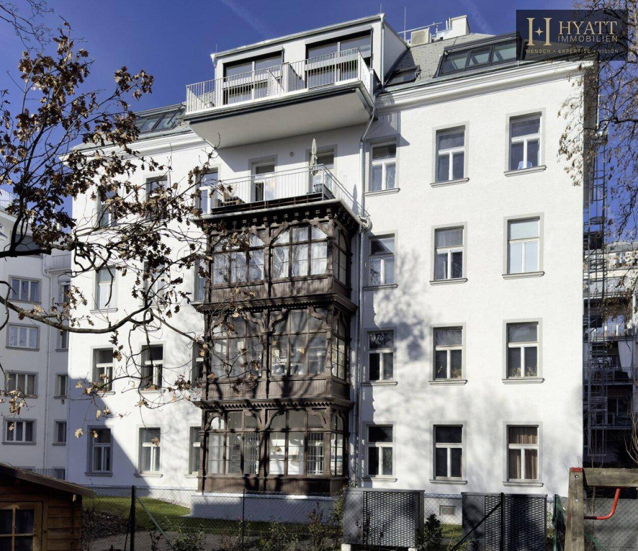 Detailansicht der weißen Fassade mit dem charakteristischen Holzerker und modernen Dachausbau.