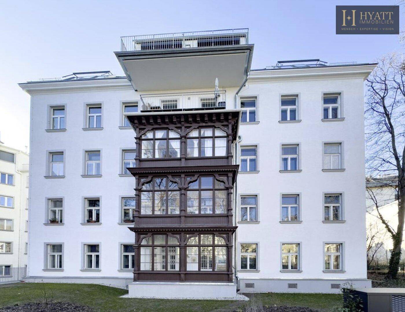Symmetrische Ansicht der Gebäudefassade mit dem dunklen Holzerker und der modernen Dachterrasse.