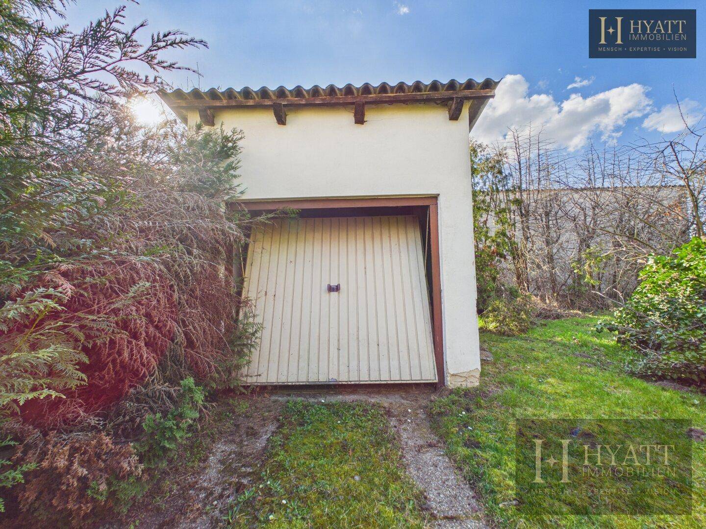 Freistehende Garage mit Holztor und Ziegeldach, umgeben von Grün.