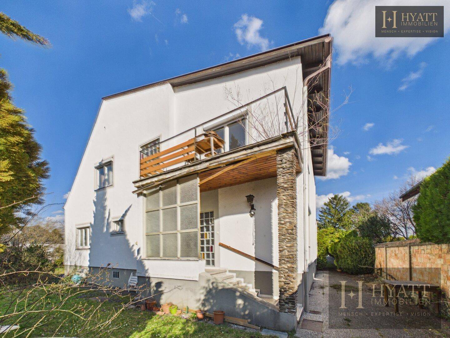 Eingangsbereich des Hauses mit Steinsäule, Balkon und Zugang zum Garten.