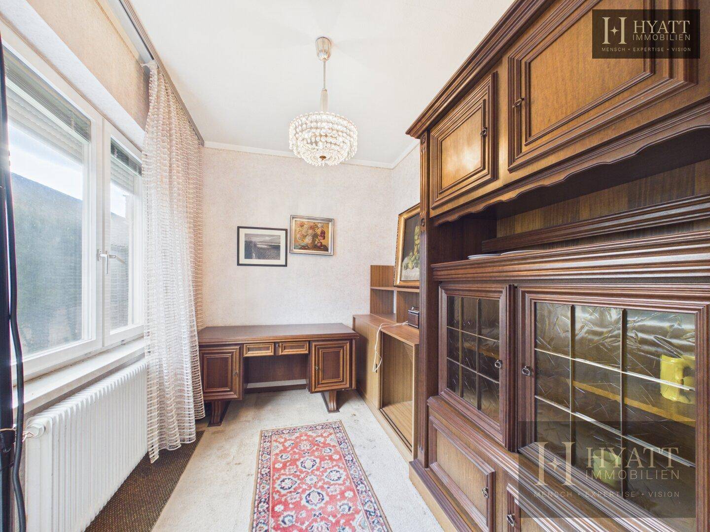 Helles Zimmer mit Schreibtisch, Holzschrank und großem Fenster, ideal als Arbeitszimmer.