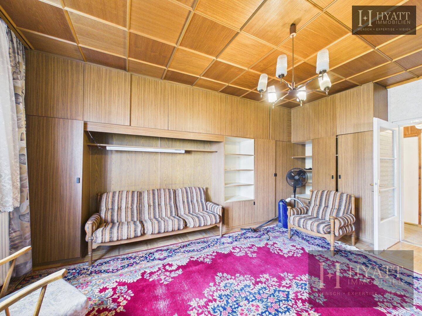 Zimmer mit Holzdecke, Einbauschränken und einem Sofa, das als Schlaf- oder Gästezimmer dienen könnte.