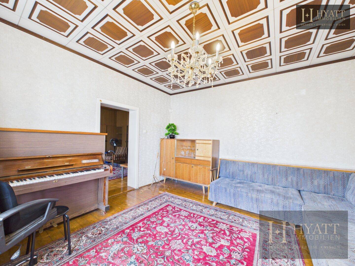 Wohnzimmer mit Klavier, Holzdecke und traditionellem Teppich, das eine gemütliche Atmosphäre schafft.