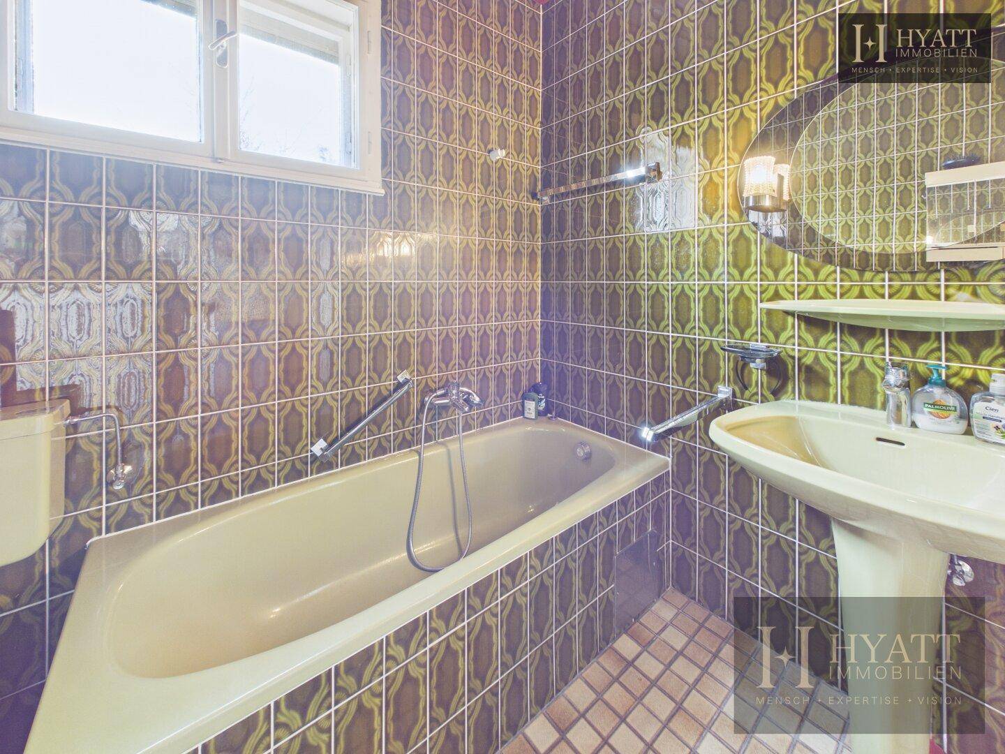 Badezimmer mit Badewanne, Waschbecken und auffälligen grünen Fliesen im Retro-Stil.