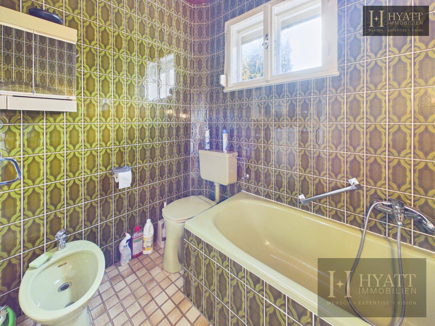 Badezimmer mit Badewanne, Toilette und Bidet, komplett gefliest in einem markanten Retro-Muster.
