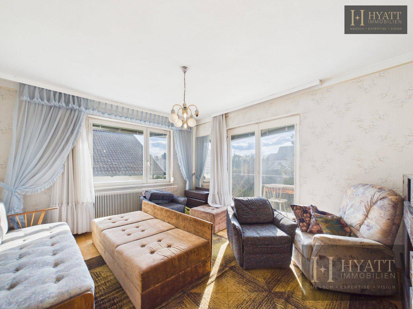 Helles Wohnzimmer mit großen Fenstern, bequemen Sofas und einem Teppich, der den Raum gemütlich macht.