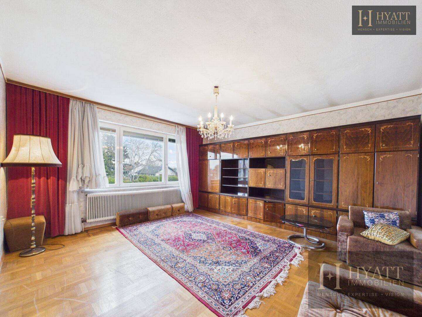 Geräumiges Wohnzimmer mit Parkettboden, großer Holzschrankwand und einem traditionellen Teppich.