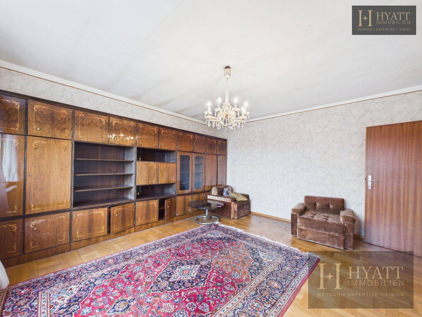 Wohnzimmer mit großer Holzschrankwand, Parkettboden und einem traditionellen Teppich, der den Raum schmückt.
