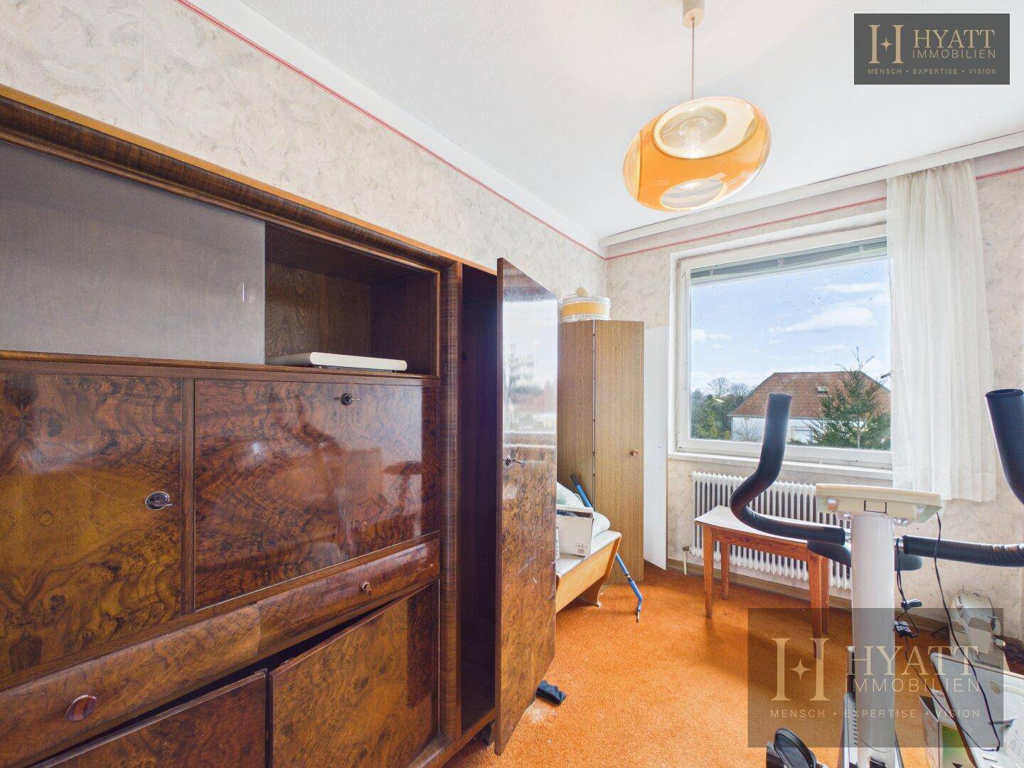 Zimmer mit Holzschrank, orangefarbenem Boden und Fenster mit Blick ins Grüne, ideal als Hobbyraum.