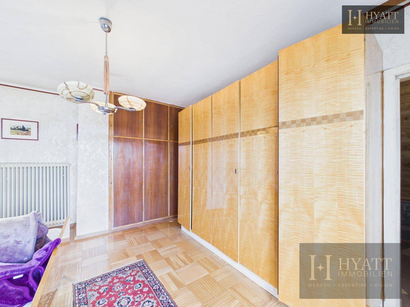Schlafzimmer mit großen Holzschränken, Parkettboden und einem Teppich, der den Raum gemütlich macht.